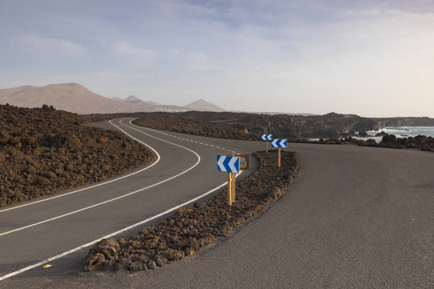 Road along Los Hervideros,rugged volcanic coastline known for waves crashing into sea caves & picturesque views.
