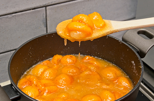 Homemade apricot jam making process - Scooping apricots with a spoon to see if sugar is dissolving