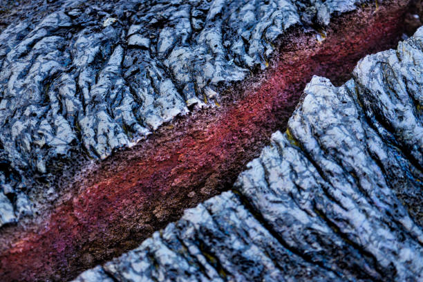 In the photo, a weathered expanse of hardened lava dominates the scene. A jagged split cuts through the black, textured surface, revealing a flash of vibrant red rock beneath.