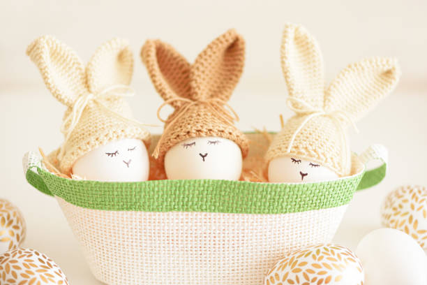 Easter eggs in crochet knitted hats with rabbit ears in nest. Easter celebration concept