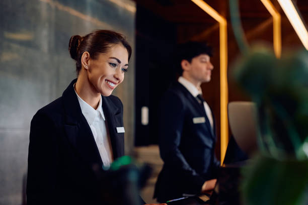 Happy female concierge working on a computer at front desk in a hotel.