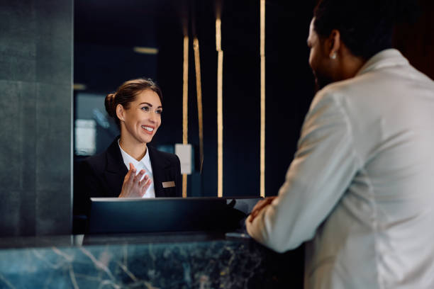 istock Happy hotel receptionist talking to a guest at front desk. 2057973598