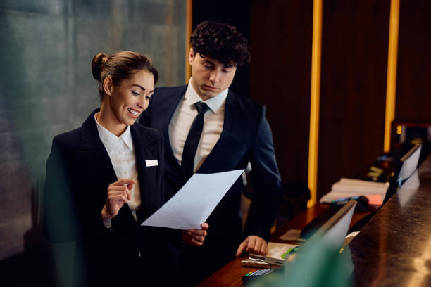 istock Happy concierge and her coworker analyzing paperwork at hotel reception desk. 2057975224