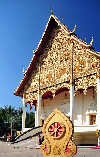 Vientiane, Laos: Wat That Luang Neua, temple on That Luang Park, Pha That Luang complex, Ban Thatluang. Wheel of Dhamma (Dharmachakra / Thammachak) Buddhist symbol framed by stylezed Nagas and façade of the congregation hall (sim).
