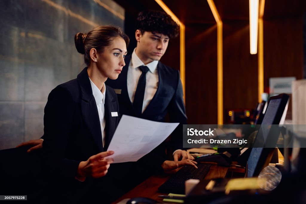 Hotel Receptionist Job Using Computer Two Receptionists Working On A Computer While Checking Documents At ...