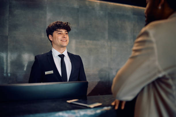 istock Happy receptionist serving a guest at hotel front desk. 2057975764
