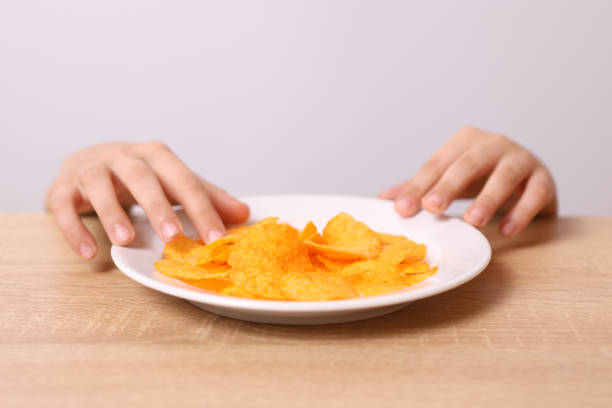 istock Children's hands are visible from under the table, trying to take potato chips from the table. 2057979083