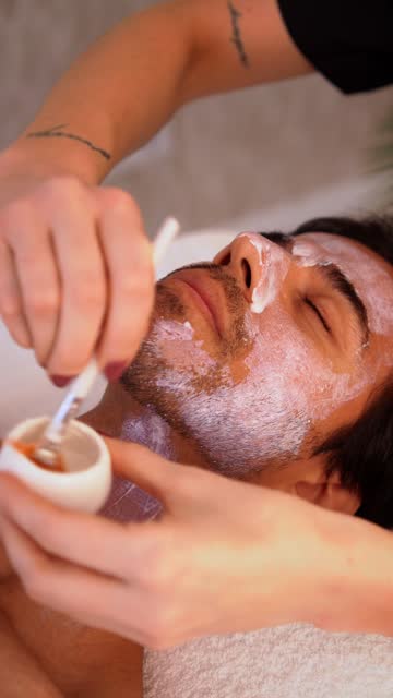 Dermatologist spreading cream to the face of a man in a beautician clinic