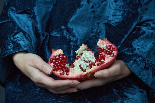 Hands holding a fresh pomegranate. Close-up shot with rich colors and textures. Healthy eating and nutrition concept.