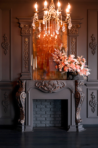 Black room interior with chandelier, mirror and fireplace decorated with flowers.