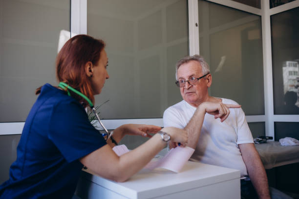 istock Happy optimistic senior 80s man looking at camera with toothy smile during appointment at doctor office. Portrait of elder male patient and young female GP therapist in background. Medic care. 2058001214