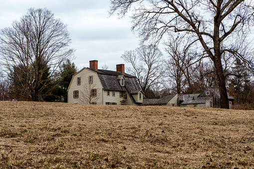 Concord, Massachusetts, USA - March 2, 2024: View across a field of the rear of the Old Manse. The Old Manse is a historic manse in Concord, Massachusetts notable for its literary associations. The Old Manse was built in 1770 for the Rev. William Emerson, father of minister William Emerson and grandfather of transcendentalist writer and lecturer Ralph Waldo Emerson. n 1842, the American writer Nathaniel Hawthorne rented the Old Manse for $100 a year. The Old Manse The house is located on Monument Street, with the Concord River just behind it. The property neighbors the North Bridge, a part of Minute Man National Historical Park. It was designated a National Historic Landmark in 1966 and is open to the public as a nonprofit museum.