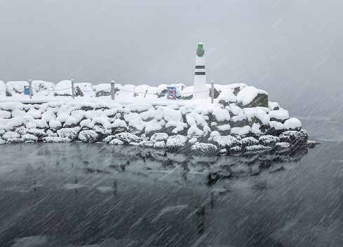 A lighthouse stands resilient as snow covers the surrounding landscape amidst a winter storm.