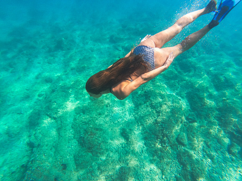 Beautiful woman wearing bikini and flippers diving under the sea towards emerald green sea bottom,  taken with underwater camera
