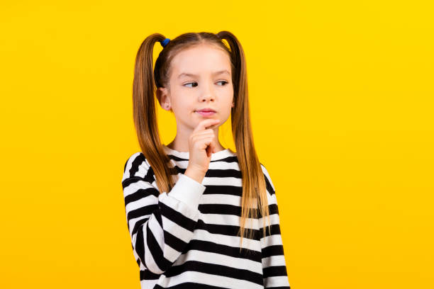 istock Photo of doubtful unsure little child dressed striped pullover arm chin looking empty space isolated yellow color background 2058083643