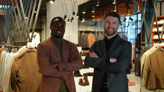 Portrait of two diverse male shoppers with crossed arms in clothing store