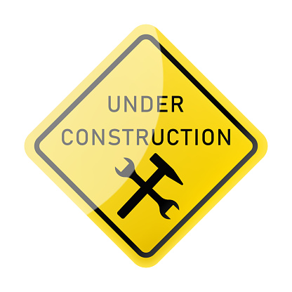Under construction sign. Under construction warning sign. Yellow sign with a crossed hammer and a wrench icon inside. Be careful at construction site. Repair work. Cars. Workshop. Machine.