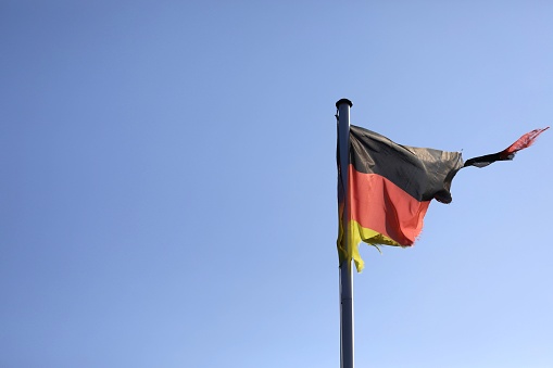 broken torn disastrous German flag on a flagpole in front of a blue sky with open space