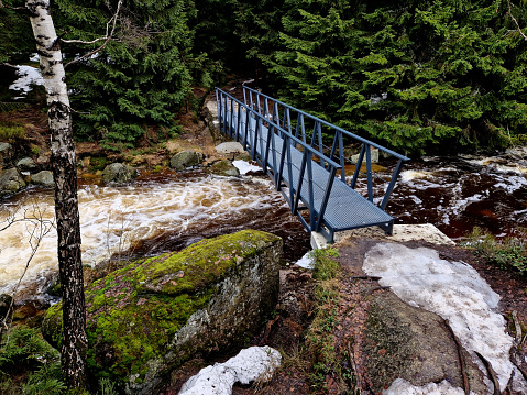 raging elements of water in a mountain river. the damaged and torn down wooden mast was washed away by the flood and crus, wedinghed against the rocks. the new metal durable bridge withstands the waves of the