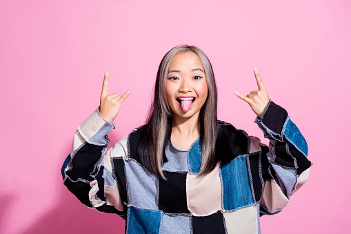 Portrait of carefree positive person tongue out arms demonstrate heavy metal symbol isolated on pink color background.