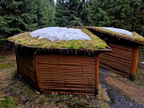 tourist shelter made of logs. a log house with a green roof covered with snow. There is a passage between the two circle-shaped pergolas. emergency sleepover in the forest.
