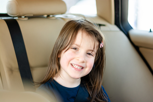 Portrait of a cute little girl is traveling in a car wearing a seat belt and looking at the camera