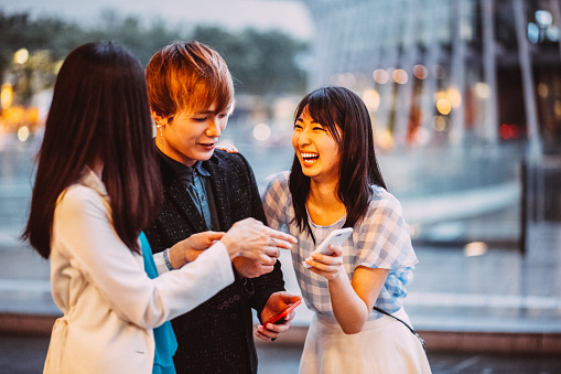 Happy friends in Osaka city using smartphone at the street