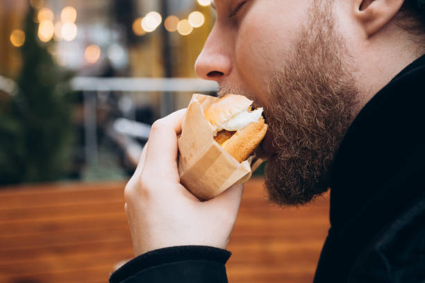 istock A young bearded man eats a burger outside against the backdrop of a cafe. 2058205456