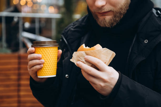 istock Bearded man with a burger and a cup of coffee outside on a blurred background. 2058205458