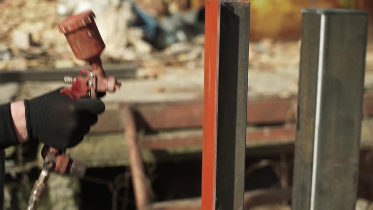 Craftsman paints a metal structure using a spray gun. Worker applies paint with paint sprayer and compressor. Slo-mo