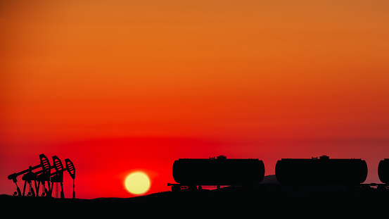 Industrial silhouette against the backdrop of a bright sunset with oil pumps and railway tanks.
