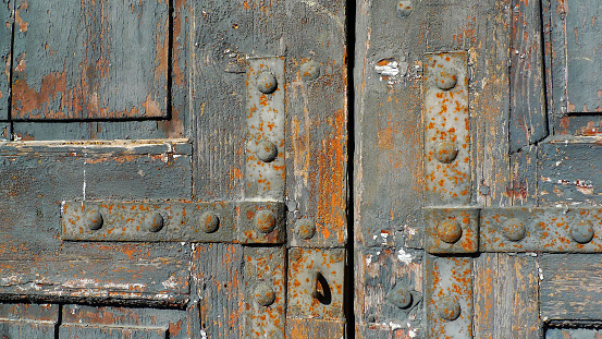 Very old, cracked wooden door with rusted hardware and peeled, ruined paint from the ravages of time