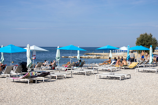 Porec, Croatia, Istria - September 30, 2023: People relaxing on the beach by the sea on a sunny day. Colorful beach umbrellas and deckchairs