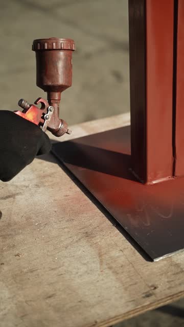 Craftsman paints a metal structure using a spray gun. Worker applies paint with paint sprayer and compressor. Slo-mo