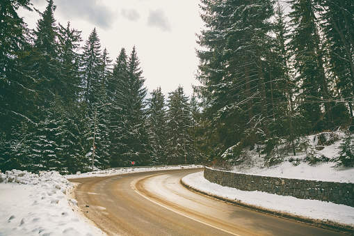 Winter idyll, bent asphalt road through the forest, high in the mountain, where sunlight and wet pavement makes glossy surface, difficult to drive.
