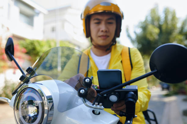 Taxi Driver Accepting Requests Man working as taxi driver sitting on motorbike and setting mobile app to accept requests from passengers vietnamese man taxi motorbike driver stock pictures, royalty-free photos & images