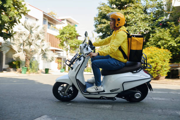 Young Man Working as Courier Side view of young man working as courier riding on motorcycle vietnamese man taxi motorbike driver stock pictures, royalty-free photos & images