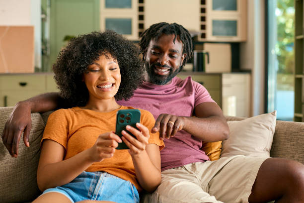 istock Couple Sitting On Sofa At Home Looking At Mobile Phone Together 2058274243