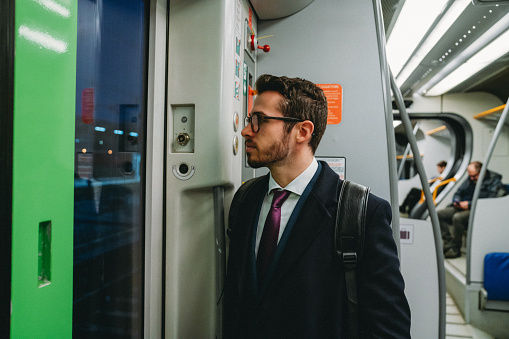 A young businessman is going to work with a train. He's wearing a suit and a coat.