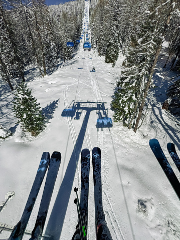 Point of view of a couple with ski sitting in chairlift at ski resort going up the snow mountain slope. Two people on the ski lift moving up the mountain.