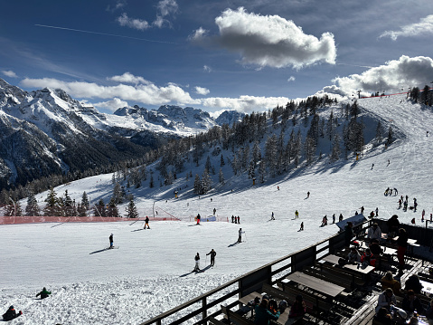 Aerial view of people enjoying skiing on the ski slope. Tourists skiing down the mountain slope on sunny winter day.