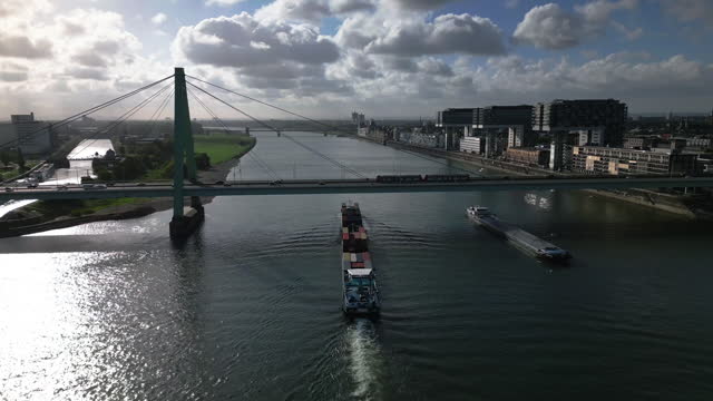 Aerial view Real time Footage of above Cargo ship carries the container traveling with speed over Rhine river with Severin Bridge (Severinsbrücke) and Rheinauhafen in  Cologne, Germany