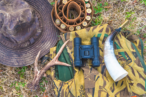 top view for hunting hat, belt with cartridges, glasses, horn and clothes on a  dry grass