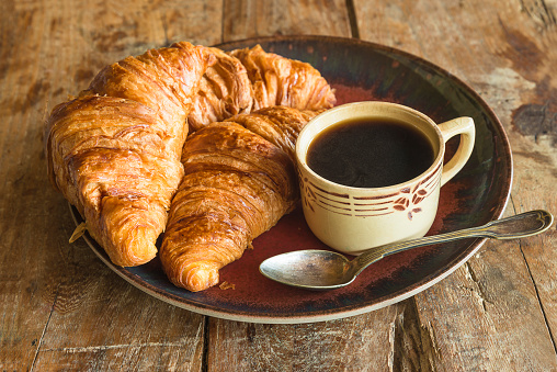 cup of coffee and hot croissants on a wooden background