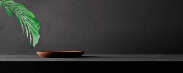 Natural wooden plate podium on black stone background with palm leaf.