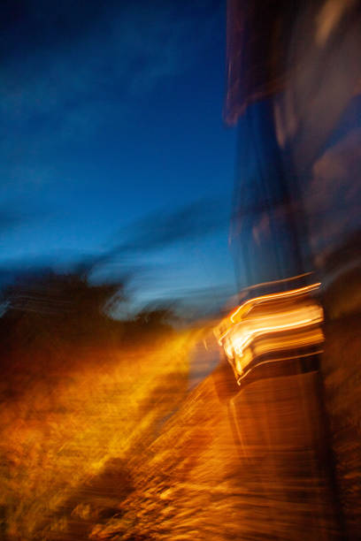 A blurry image of a car with its headlights on in the night. The car is on a dirt road and the sky is blue