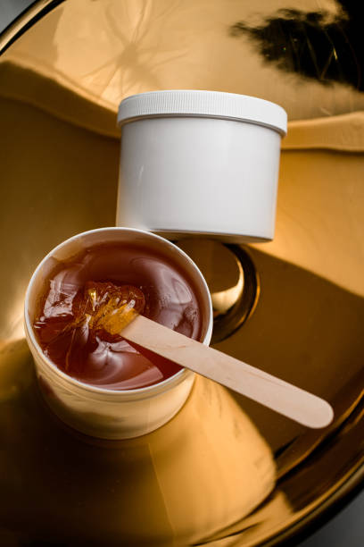 istock Brown sugaring paste or wax honey in a plastic container with a wooden spatula 2058333495