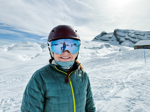 Portrait of smiling mature woman skier at a ski resort. Mid adult woman with skiing glasses with helmet looking at camera at ski resort.