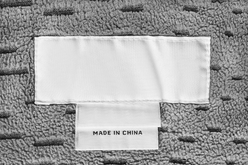 Blank clothes label says made in China stitched on grey fleece fabric closeup