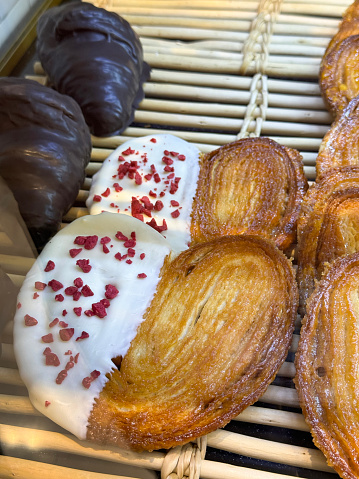 Stock photo showing close-up, elevated view of bakery shelf display with rows of freshly baked heart shaped, palmier pastries dipped in white chocolate and sprinkled with dehydrated raspberry pieces, available for purchasing.